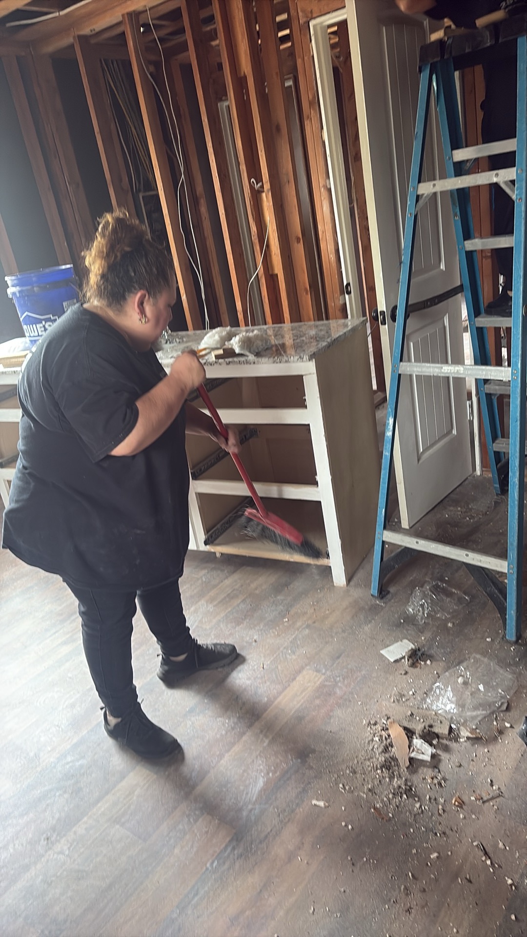 A restoration technician sweeping debris from fire damage around a cabinet base during cleanup.