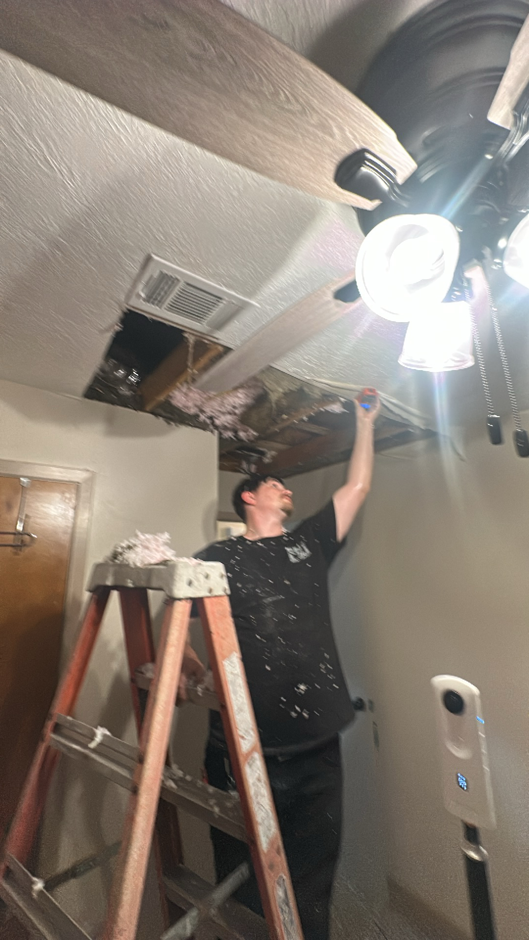 Restoration technician on a ladder inspecting structural framing after a severe ceiling collapse.