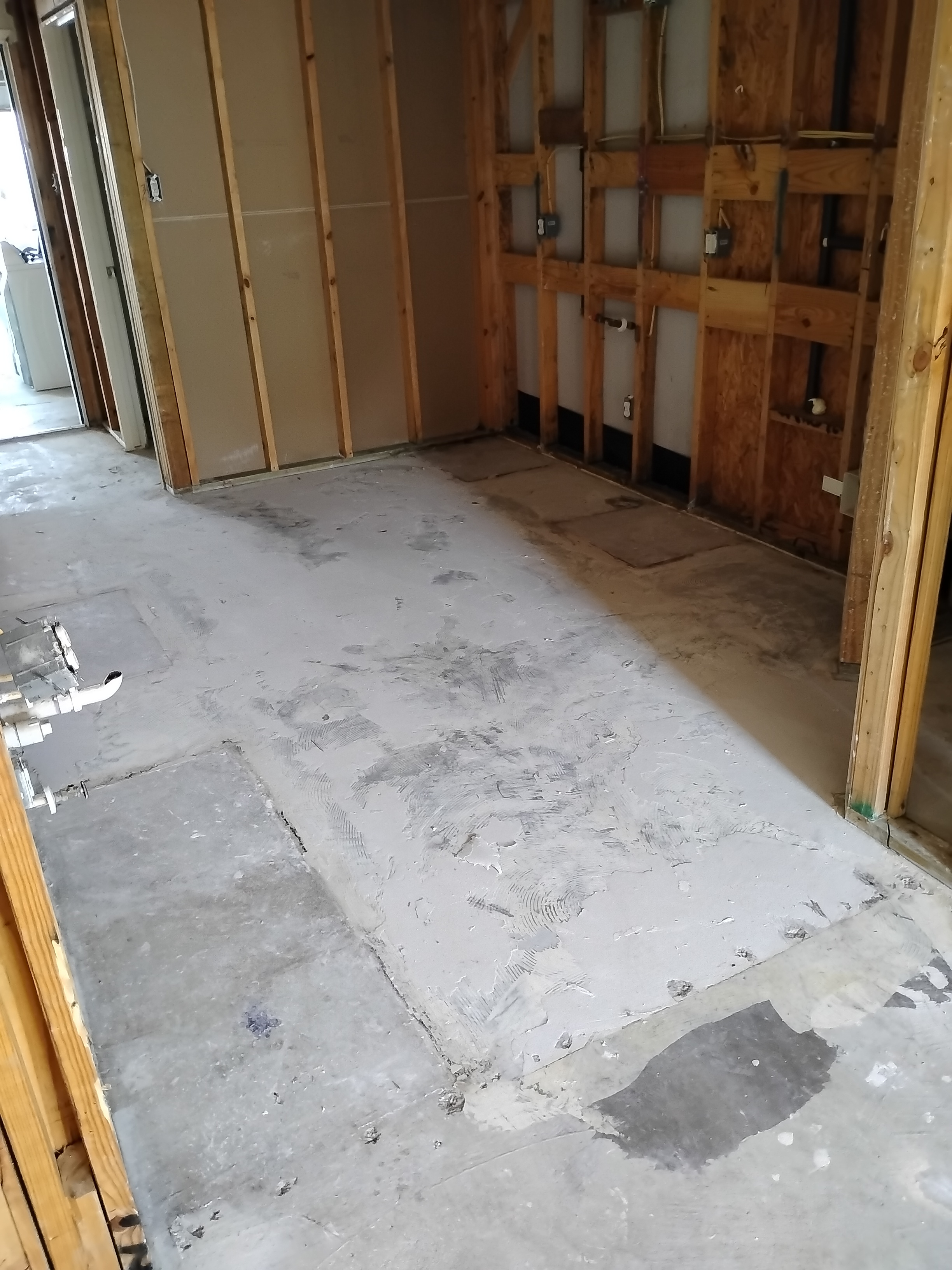 Room undergoing water damage restoration with exposed wooden studs and concrete subfloor after demolition of damaged materials.