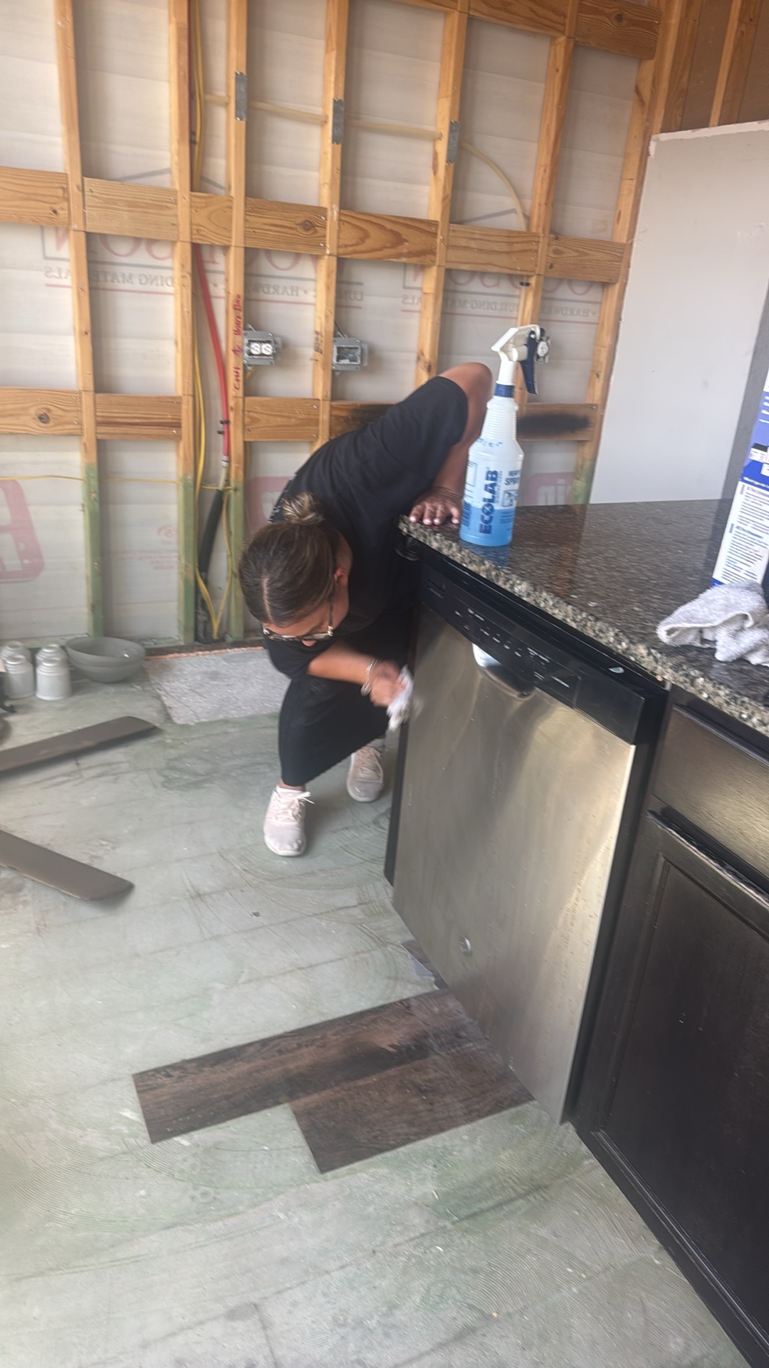 Technician cleaning a stainless steel dishwasher during kitchen fire damage restoration, with exposed wall studs in the background