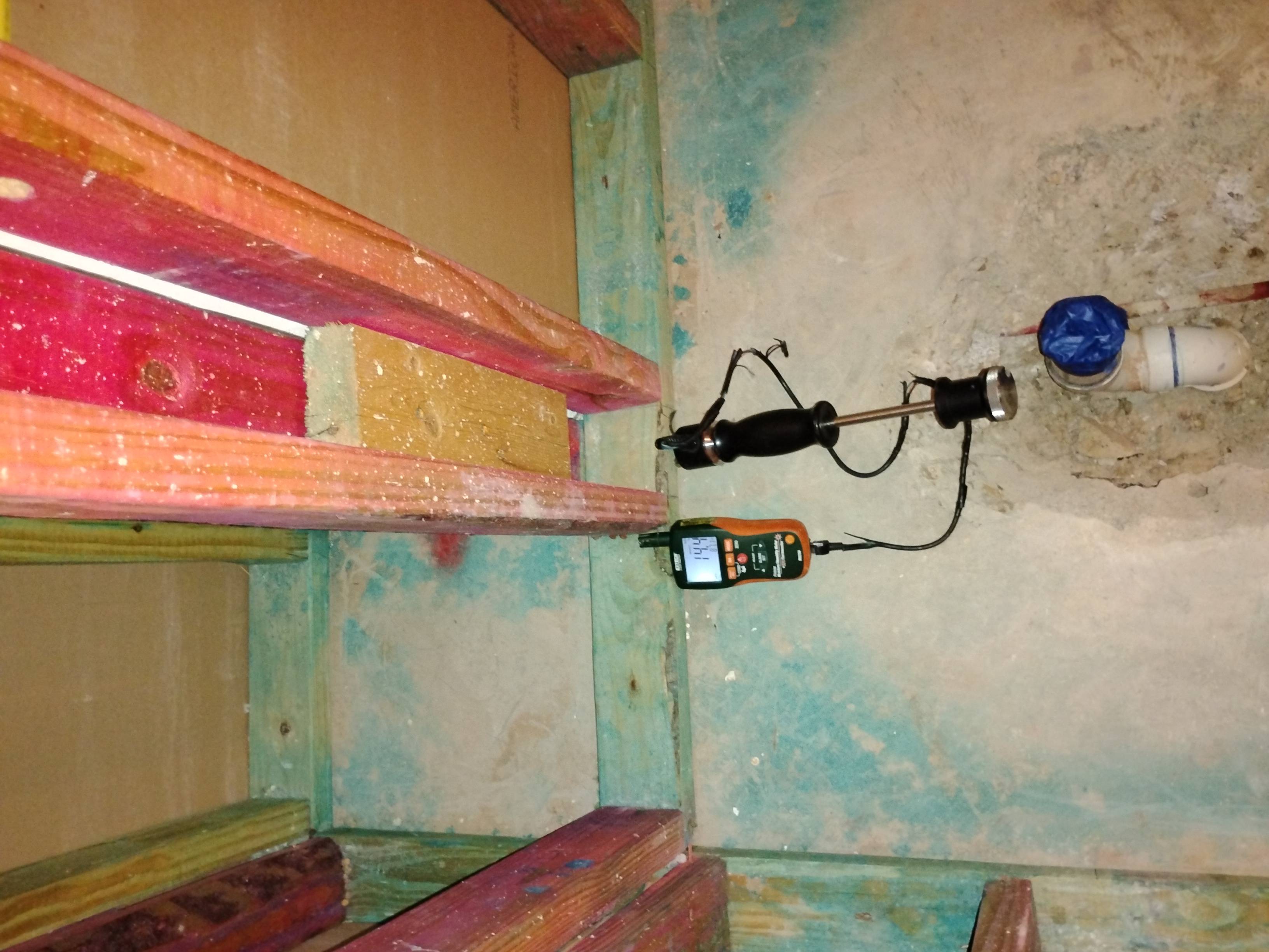 Moisture meter with a probe inserted into a subfloor or wall cavity showing a reading of 14.4, indicating hidden moisture from water damage.