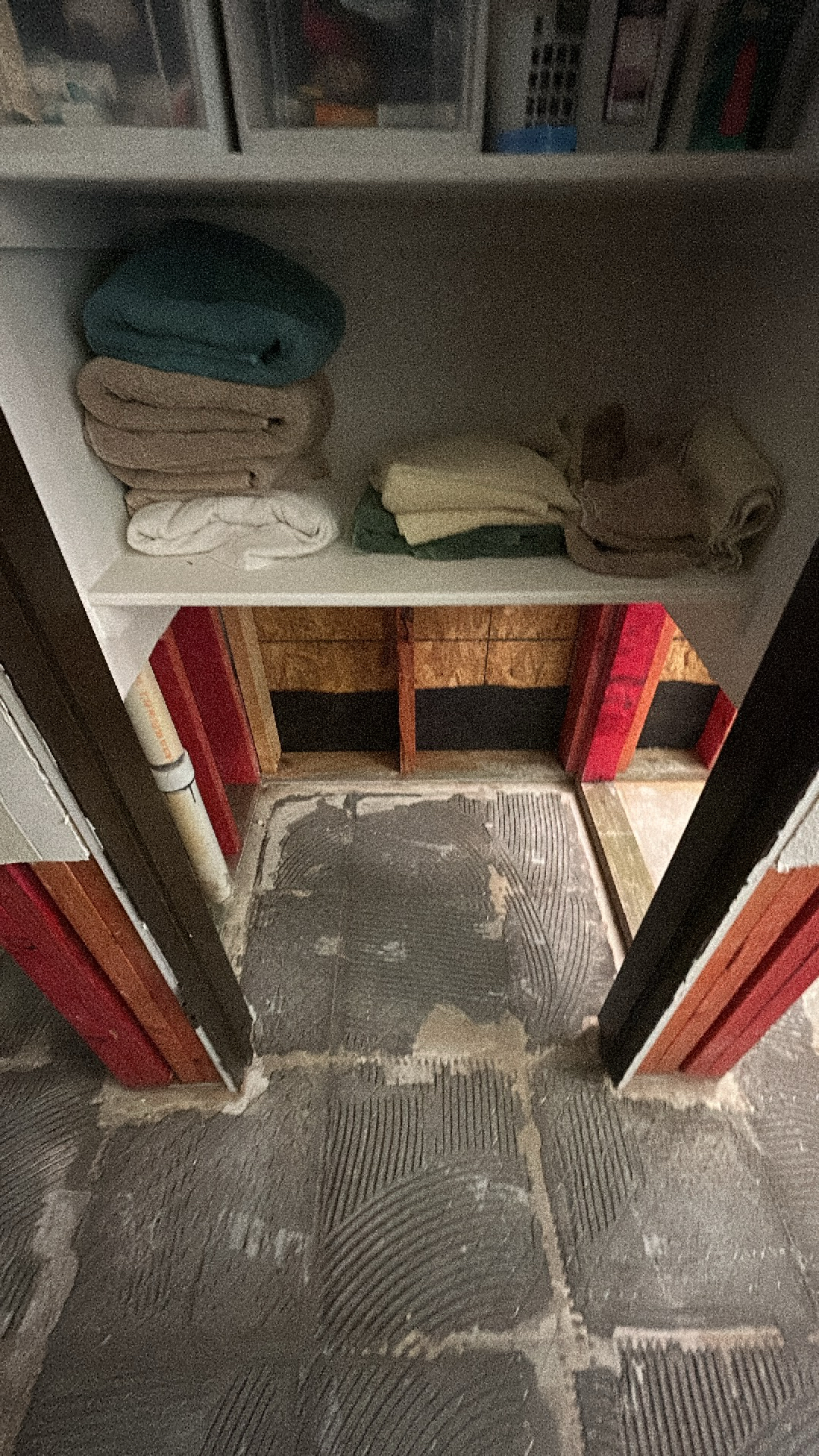 Close-up of a demolished bathroom subfloor with exposed studs and adhesive residue, showing the initial stages of water damage drying.