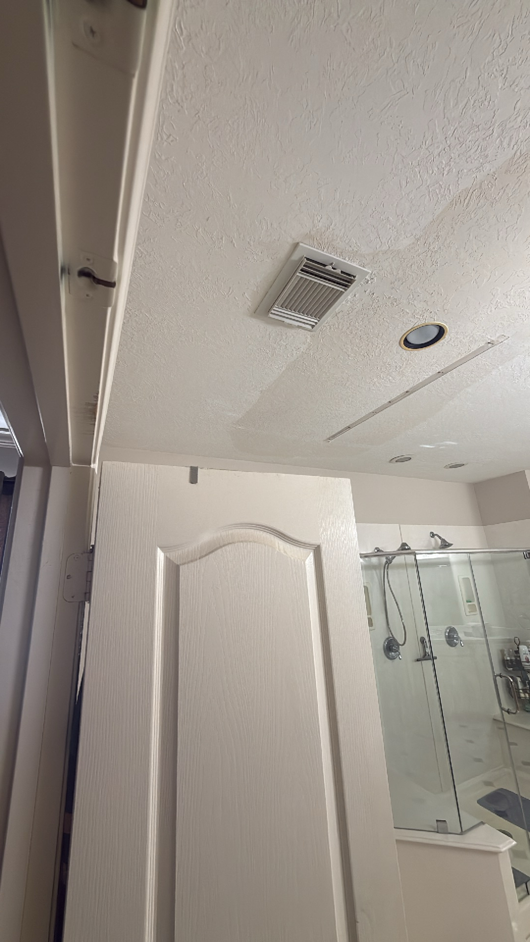 Water damage evident on a textured bathroom ceiling, showing stains near an exhaust vent, with a white door removed during restoration.