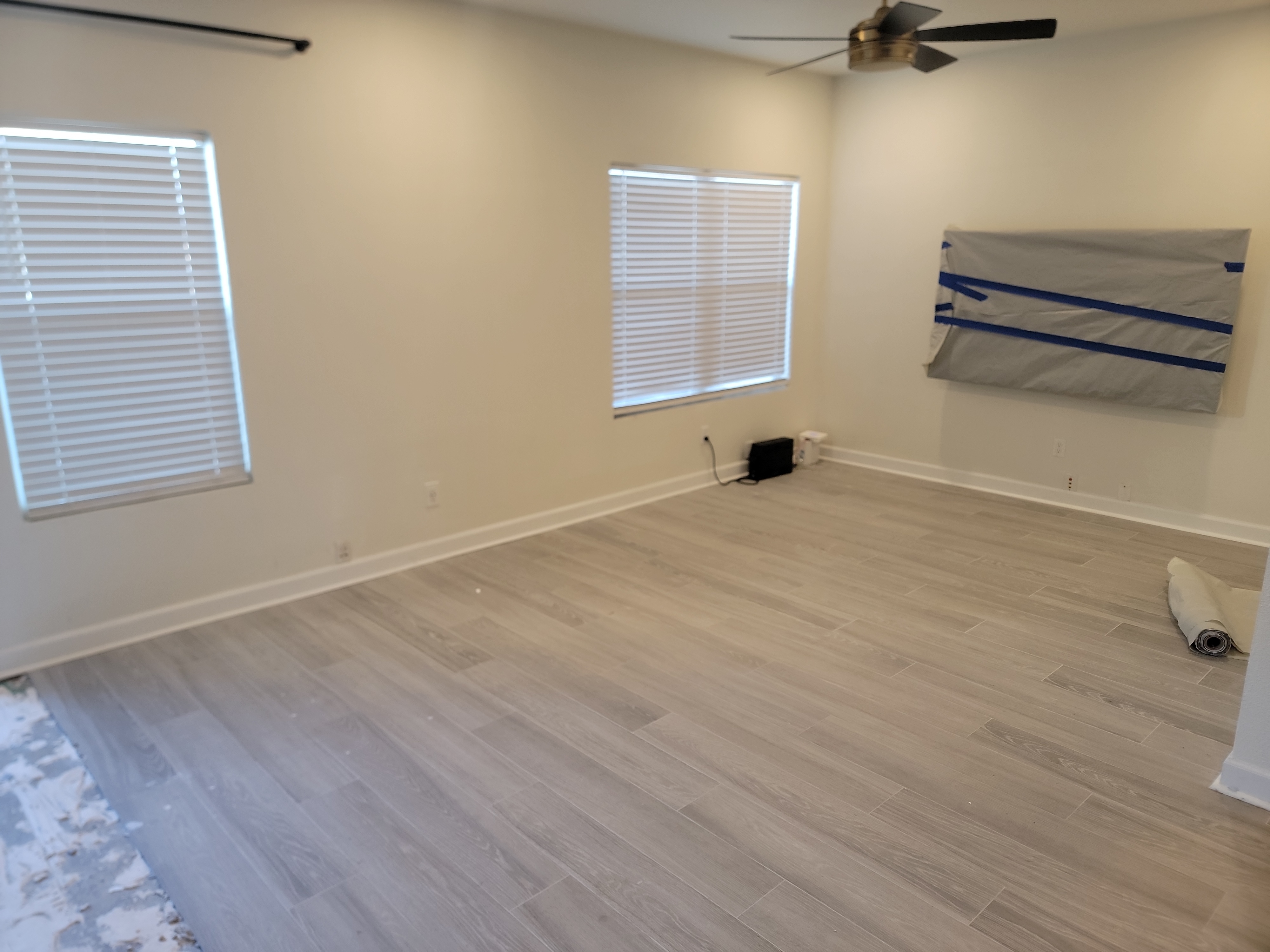 A wide view of a room showcasing newly installed light grey wood-look tile flooring, part of a comprehensive water damage restoration project.